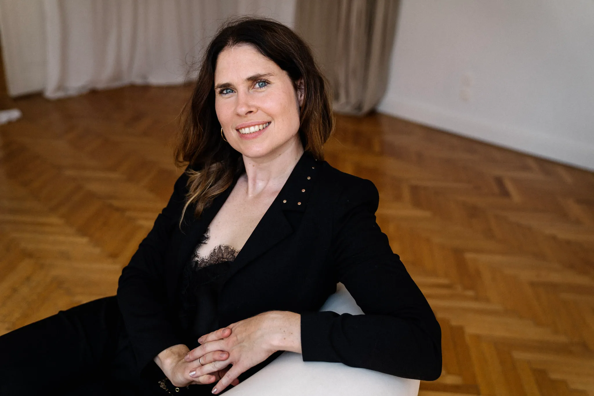 Christina Stix-Pusswald sitzt lächelnd auf Holzboden vor Vorhang, Gründerin von Webglow Webdesign