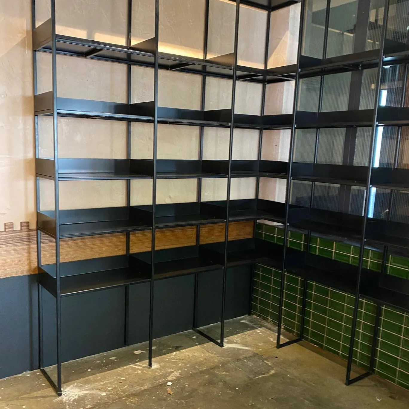 Tall metal shelving units wrapping around an internal corner with green tiled walls