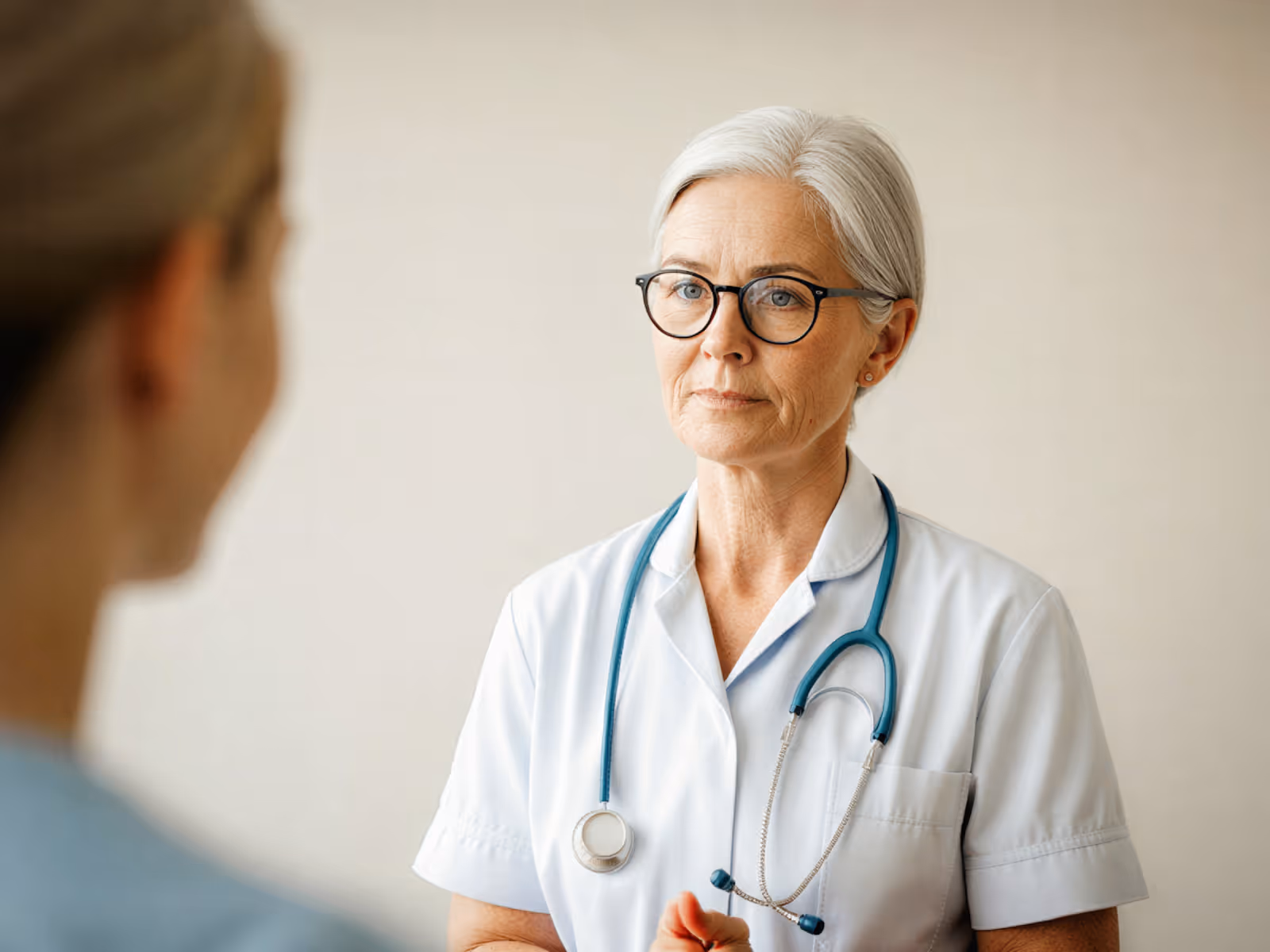 Serious female doctor with glasses and stethoscope talking to a patient.