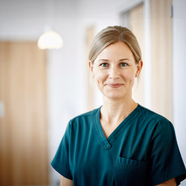 Smiling female healthcare worker wearing teal scrubs in a bright, professional setting.