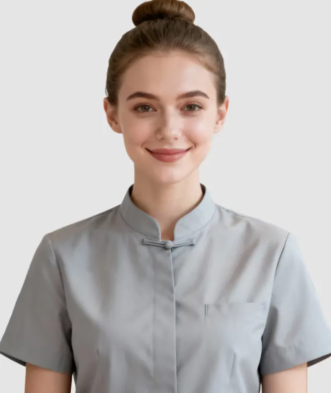 Smiling woman with hair bun wearing a gray shirt with a stand collar against a plain background.