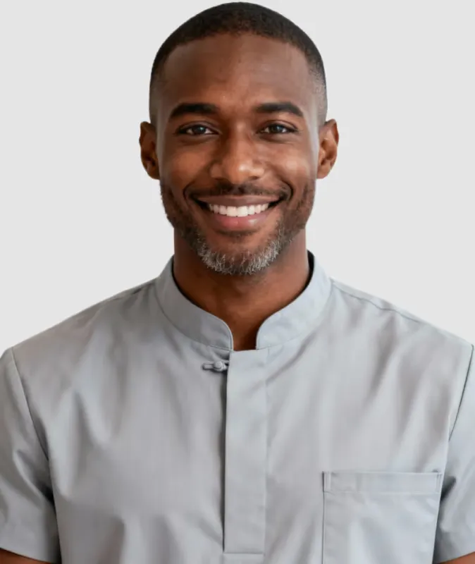 Smiling man in a gray buttoned shirt standing against a plain light background.