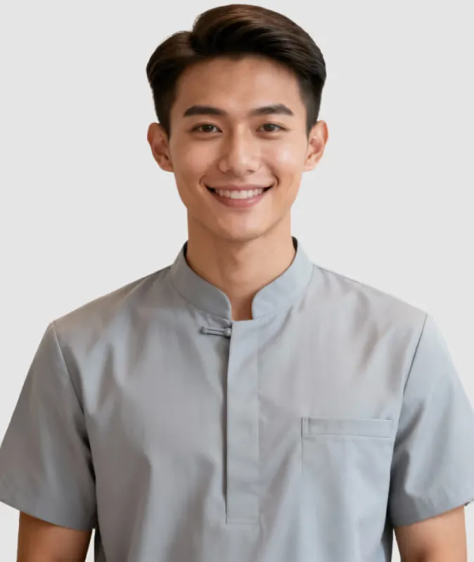 Smiling young man wearing a short-sleeved gray shirt with a mandarin collar against white background.