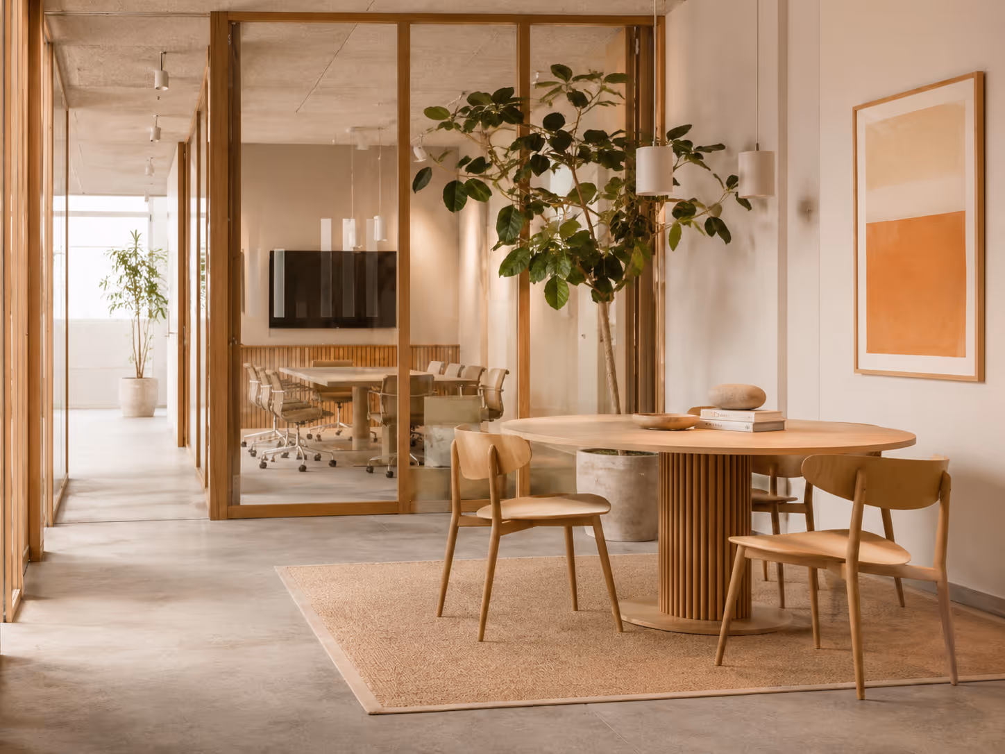 Modern office space with wooden table, three chairs, large plant, and glass-walled conference room.