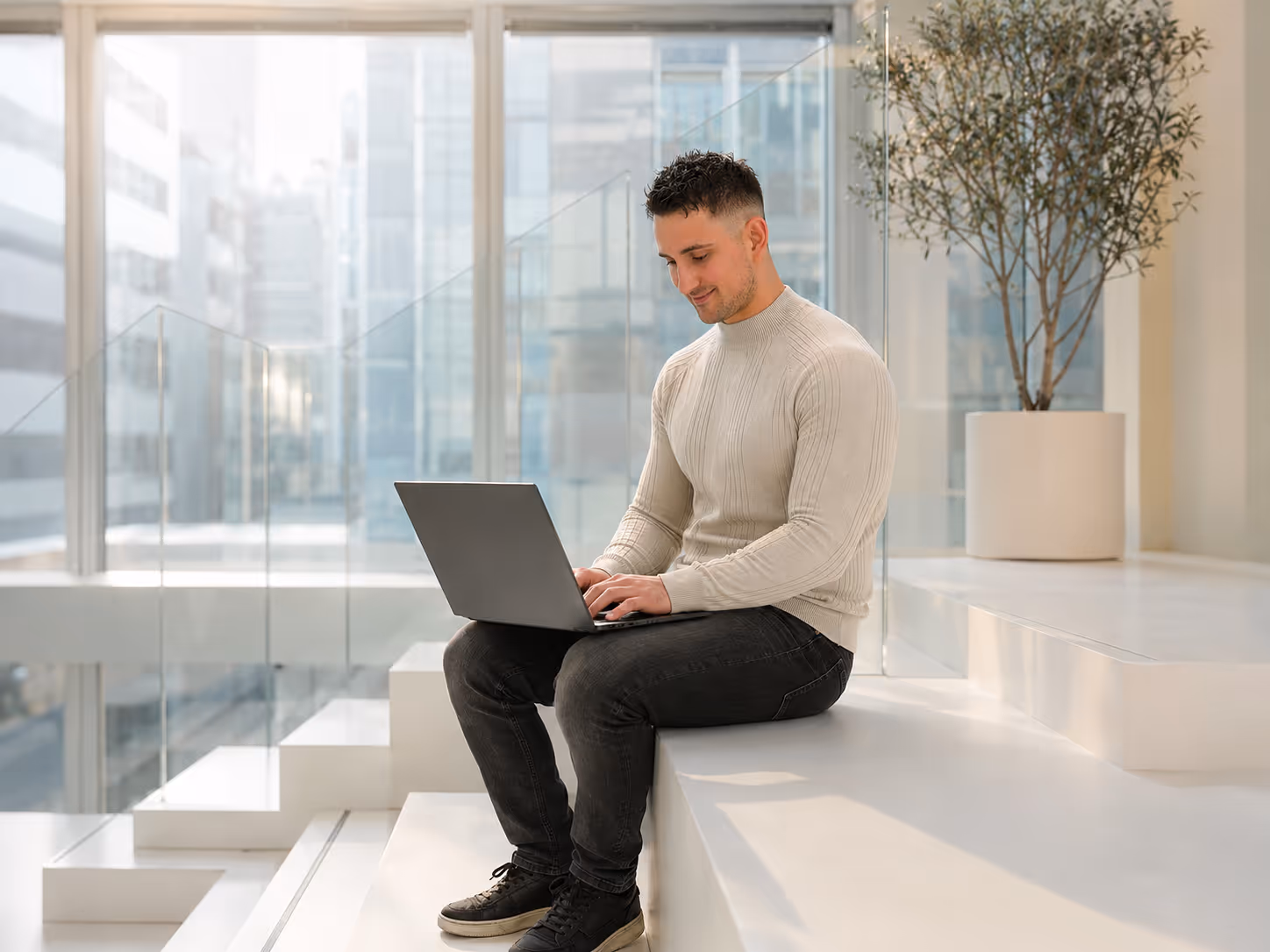 Damir from Shopcanvas sitting on white stairs working on a laptop in a bright modern space.