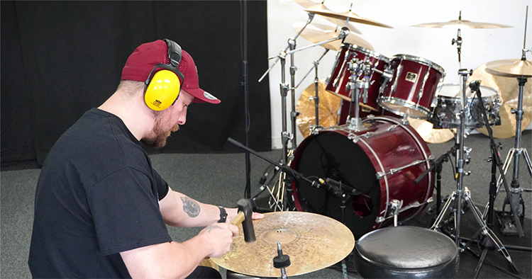 Person hammering a cymbal during the Make Your Own Cymbal experience in Bristol