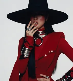 Fashion model in a red outfit and large black hat posing with rings and metal bracelets.