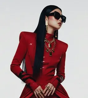 Woman with long black hair in red dress, wearing black sunglasses and gold jewelry.