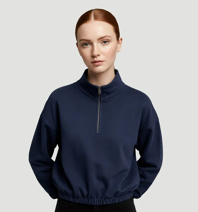 Young woman with red hair wearing a navy blue zip-up sweatshirt with elastic hem posing against gray background.