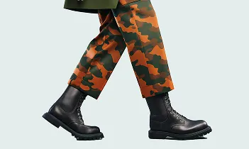 Person walking wearing black combat boots and orange-green camouflage pants.