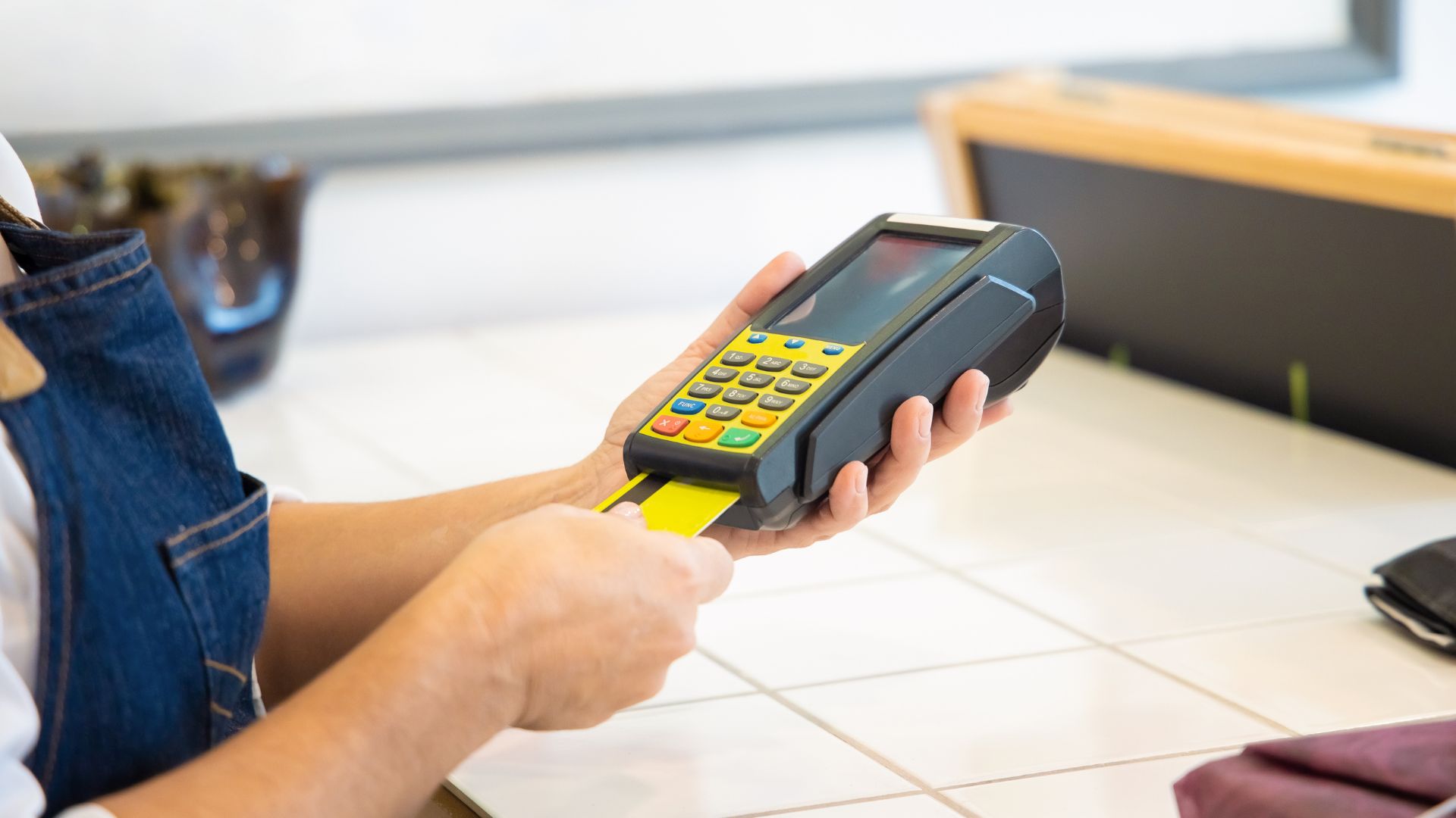 Customer inserting a yellow card into a handheld POS payment terminal at a counter