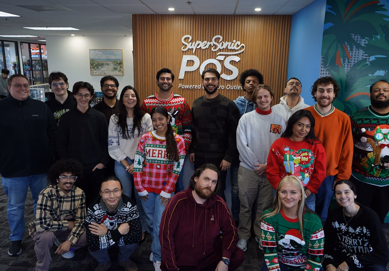 SuperSonic POS team in Christmas sweaters posing in front of the company sign