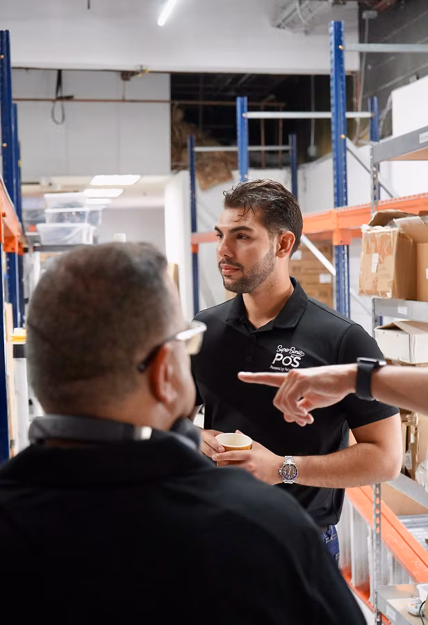 SuperSonic POS employee in a branded polo talking with a colleague in a warehouse stockroom