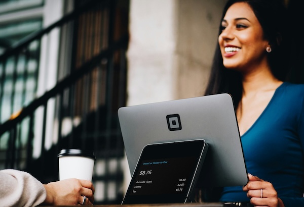 Smiling woman paying with a Square card reader at an outdoor cafe table