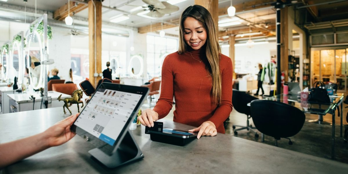Smiling woman paying by card at a SuperSonic POS tablet checkout in a boutique
