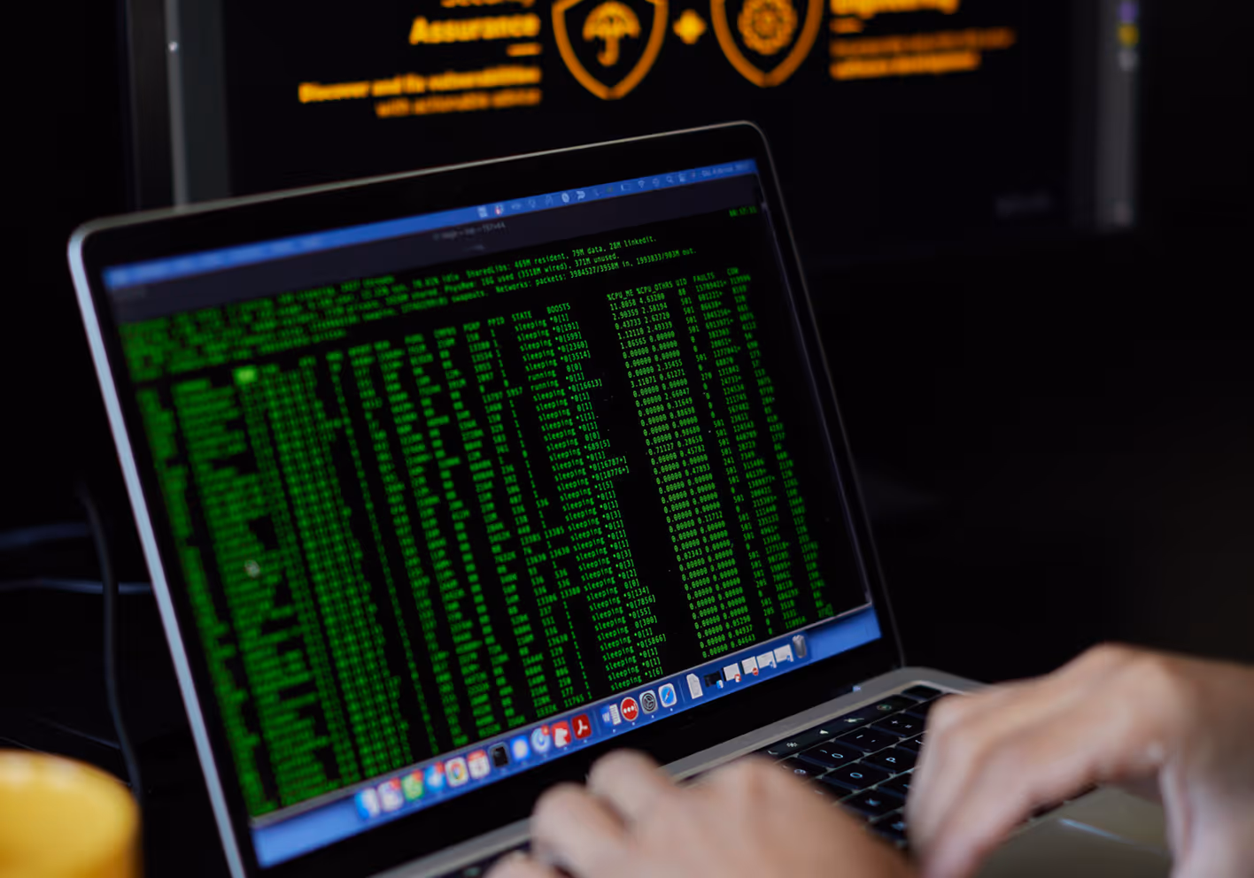 Hands typing on a laptop keyboard displaying green text in a terminal or code editor.