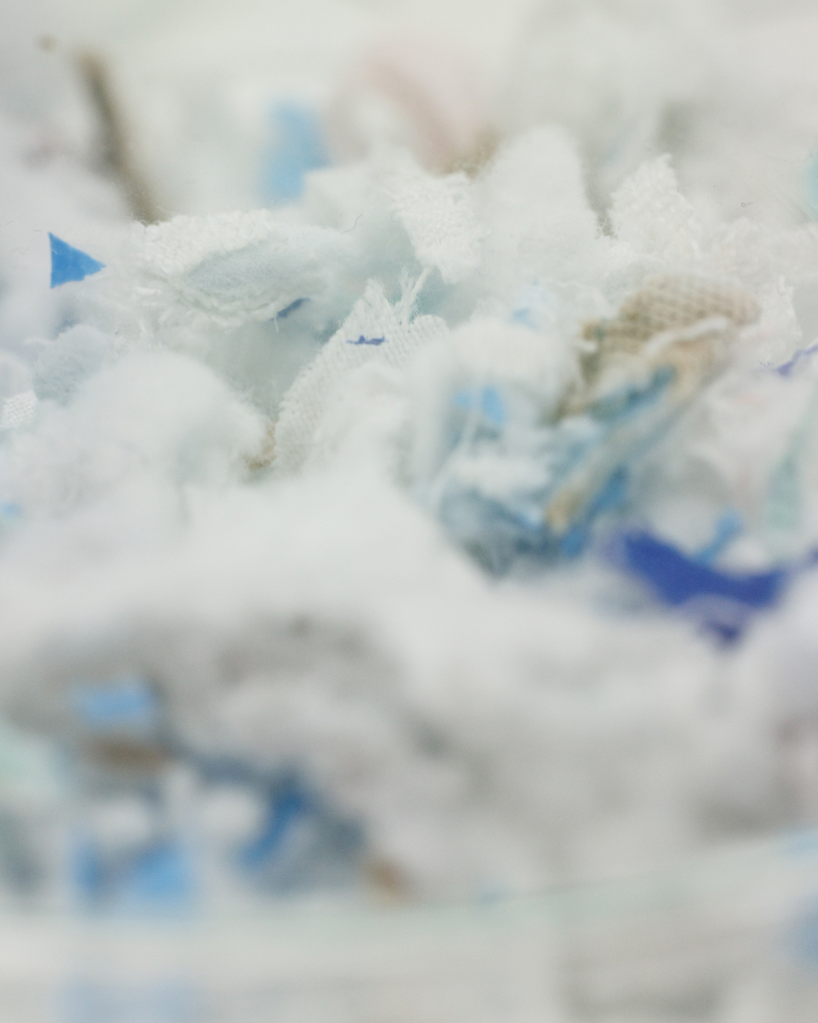 Close-up of a pile of shredded fabric pieces in white, blue, and beige colors.