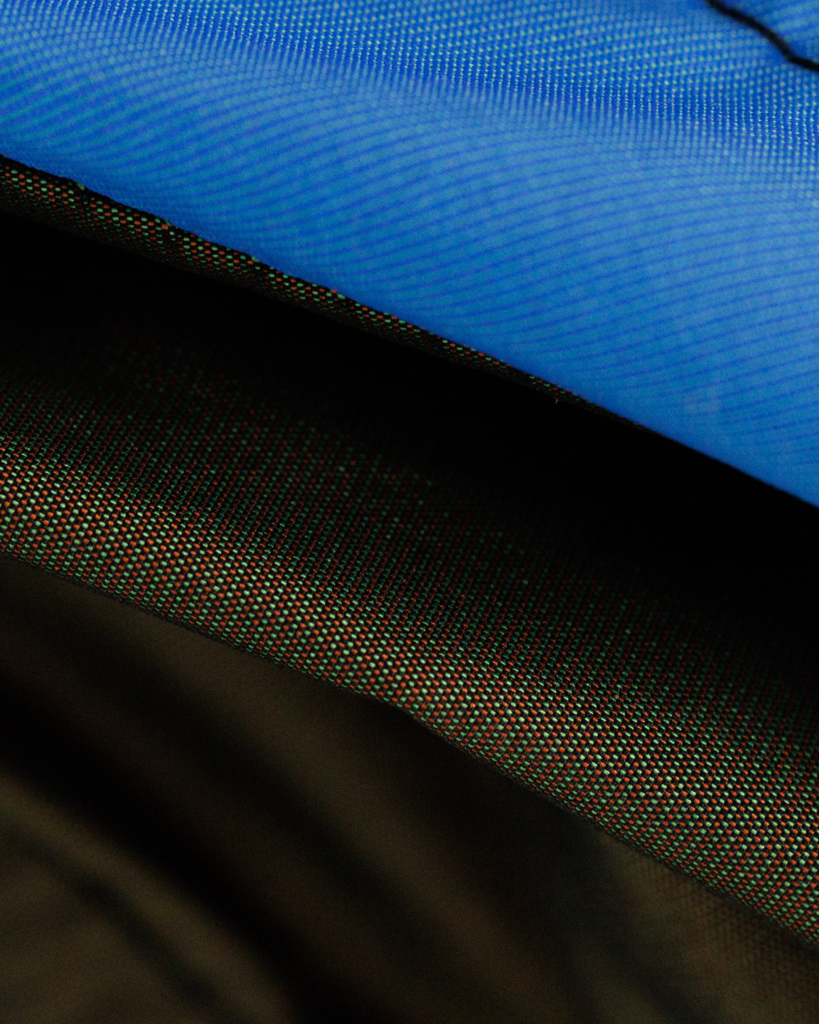 Close-up of fabric textures featuring a blue synthetic textile above a tightly woven dark fabric with red and green threads.