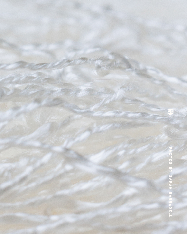 Close-up of delicate white twisted threads woven loosely over a soft, light background.