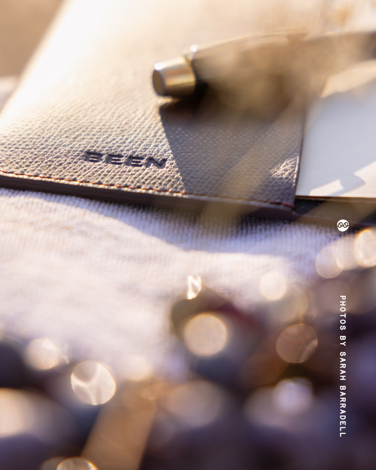 Close-up of a textured leather surface embossed with the word 'BEEN' and a pen resting on it, with soft bokeh lights in the foreground.