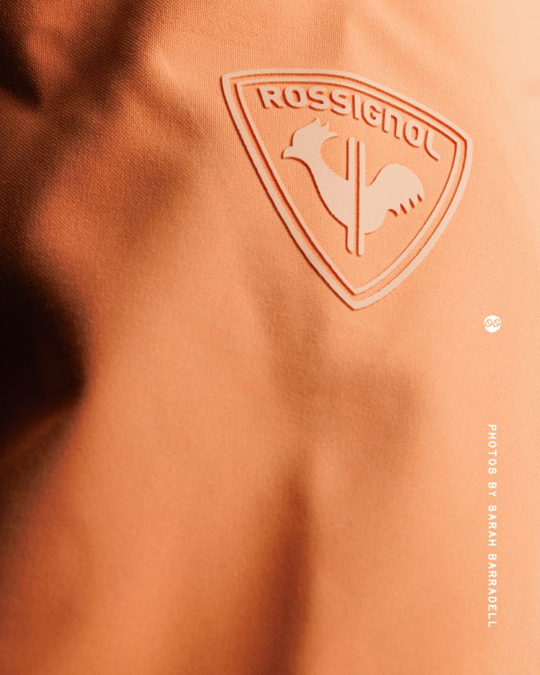 Close-up of an orange fabric with an embossed Rossignol logo featuring a rooster inside a shield shape.