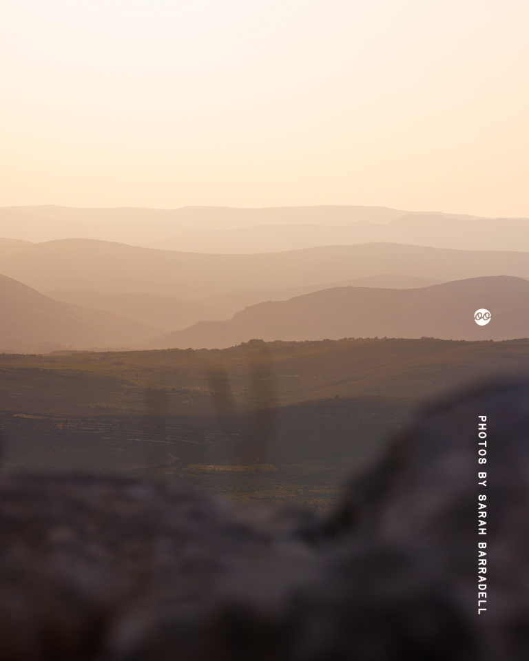 Softly layered mountain ranges fading into the distance under a pale, glowing sky, with blurred foreground rocks.