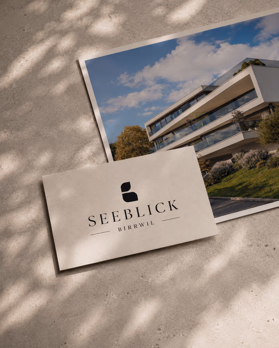 Business card with Seeblick Birrwil logo placed on top of a postcard of a modern house under blue sky.