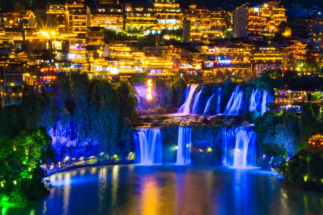 Furong Ancient Town con su cascada iluminada de azul por la noche, China