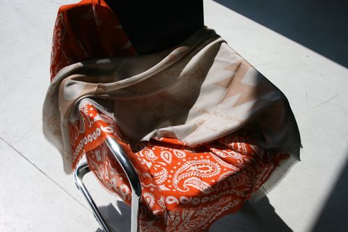 Chrome chair with orange and beige scarves with patterns draped over it in sunlight.