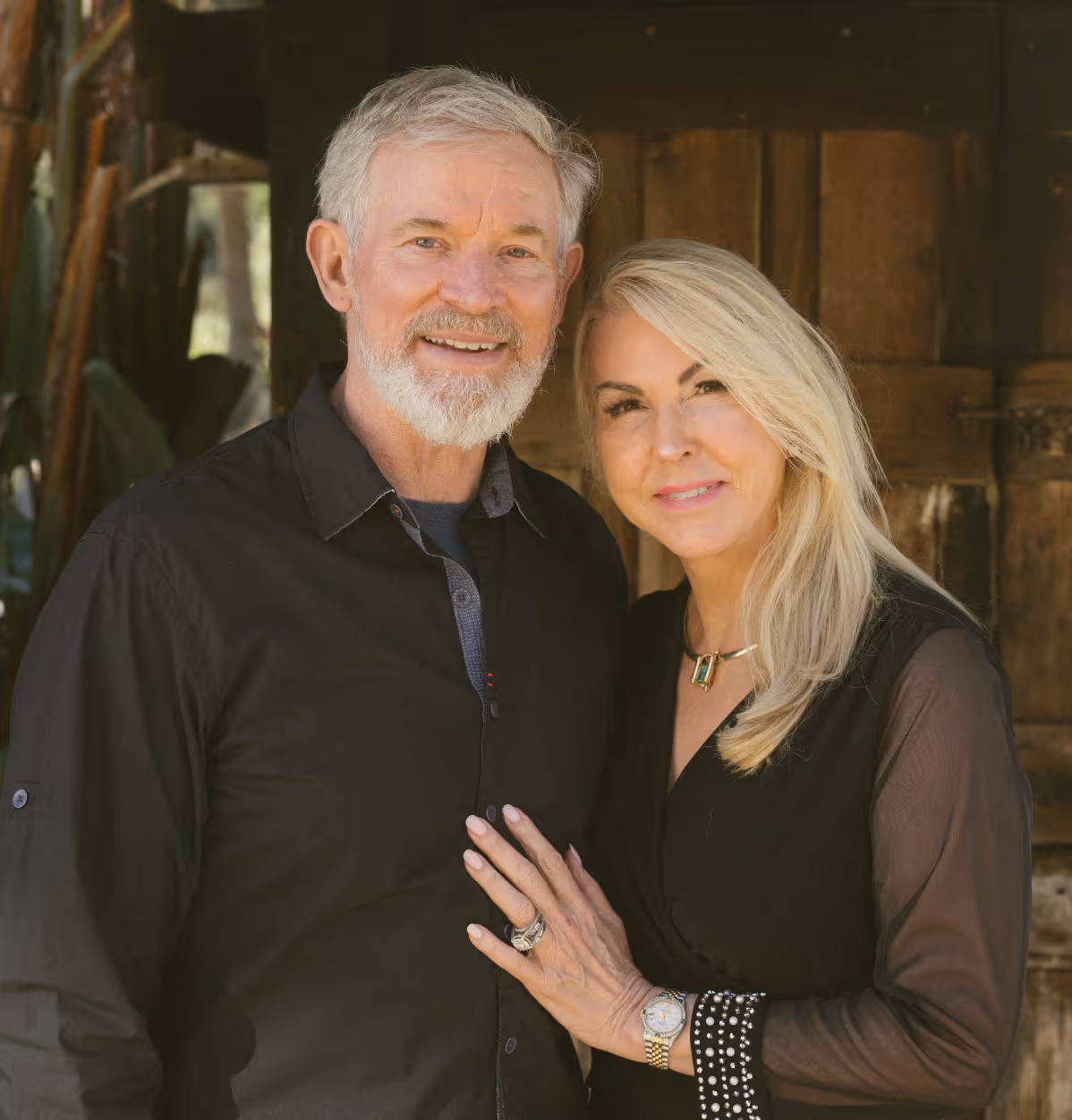 Smiling older couple posing close together, the woman has her hand on the man's chest.