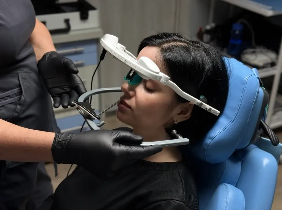 Woman in a blue dental chair wearing dental face scanner held by a person with black gloves.