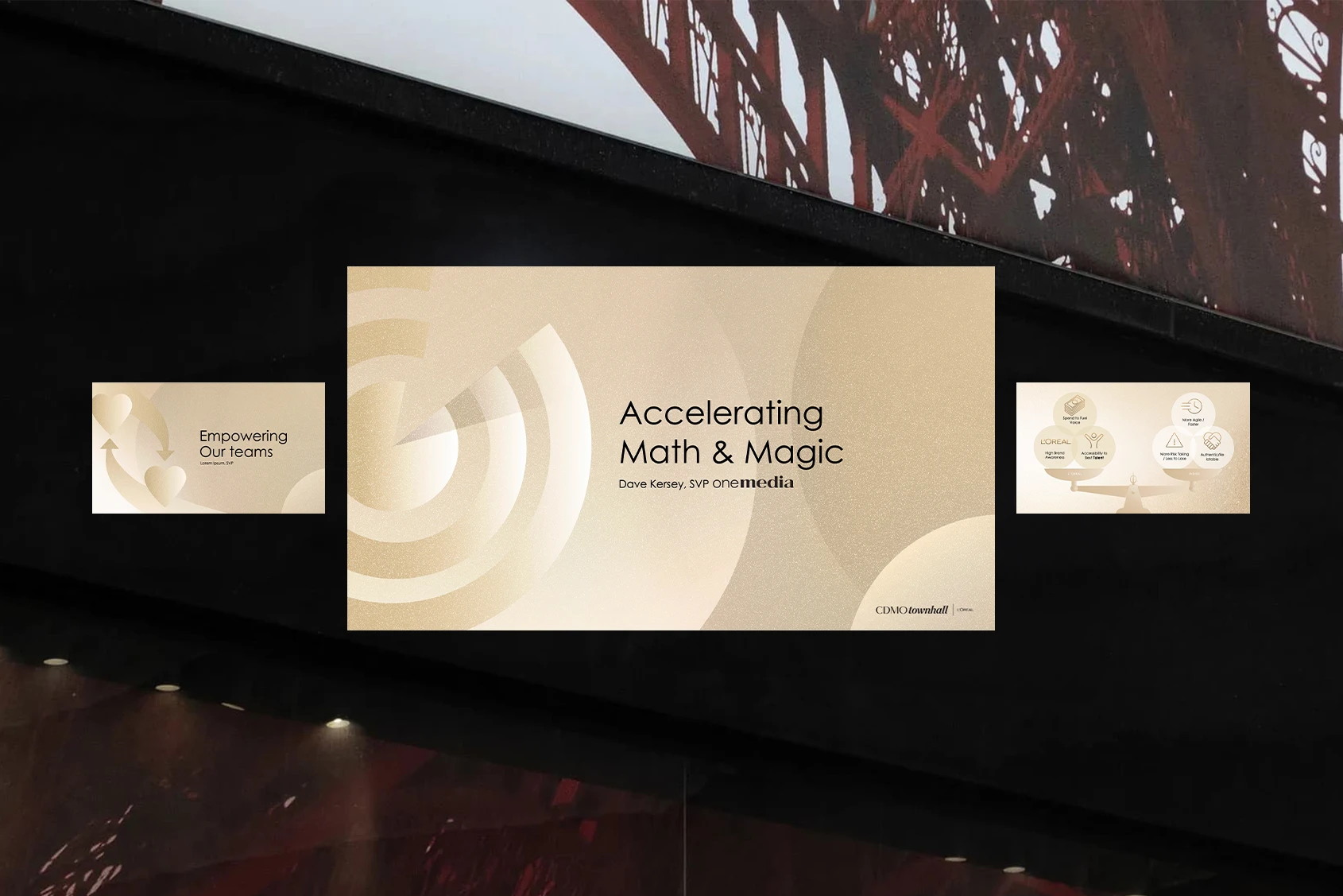 Three presentation slides displayed on large screens at the L'Oréal CDMO Townhall event, showing the gold and cream branded deck in a live venue setting with the "Accelerating Math & Magic" keynote slide centered on the main screen.