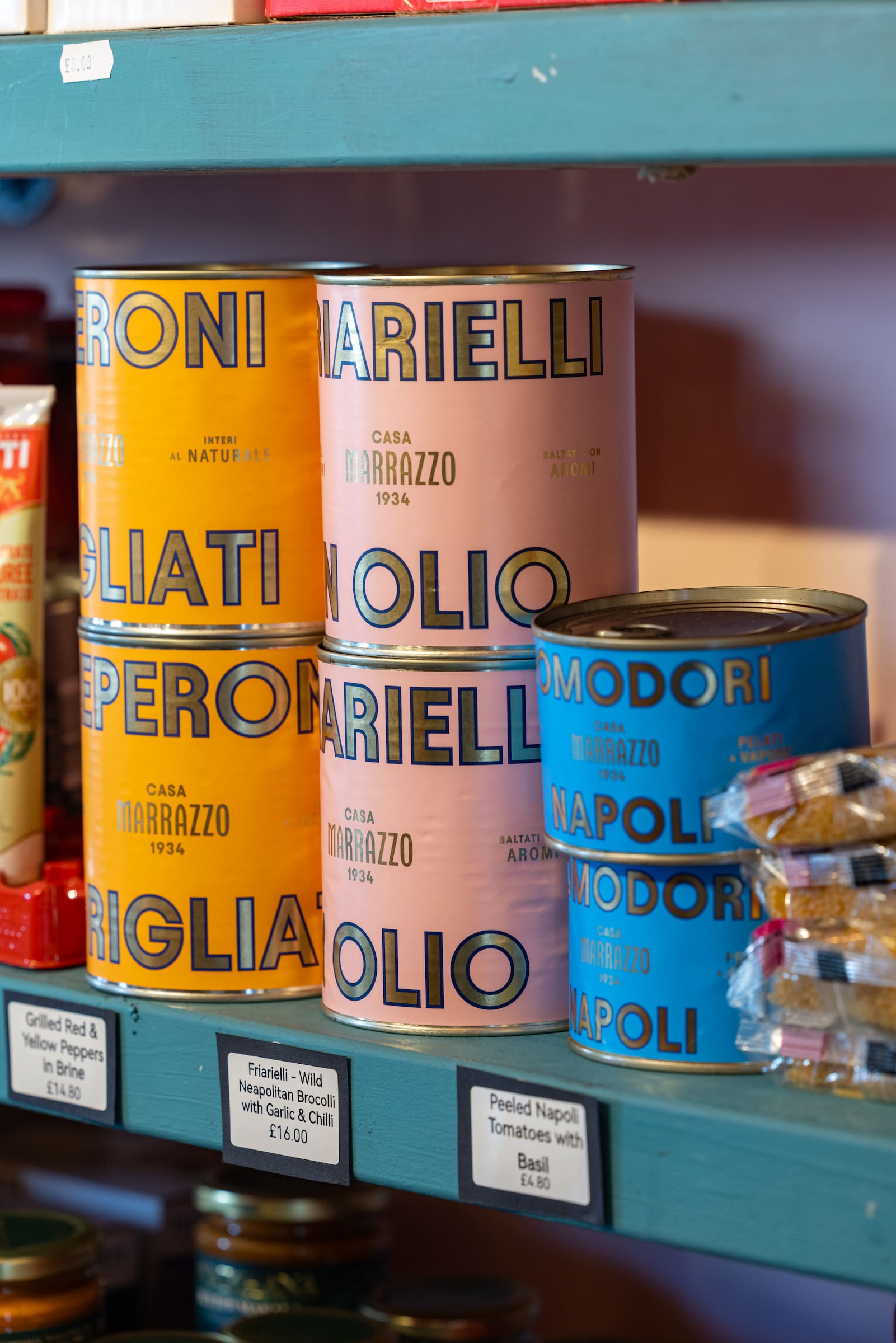 Colourful Italian deli tins from Casa Marrazzo stacked on teal painted shelves at Basil and Tom's grocery shop in Acton