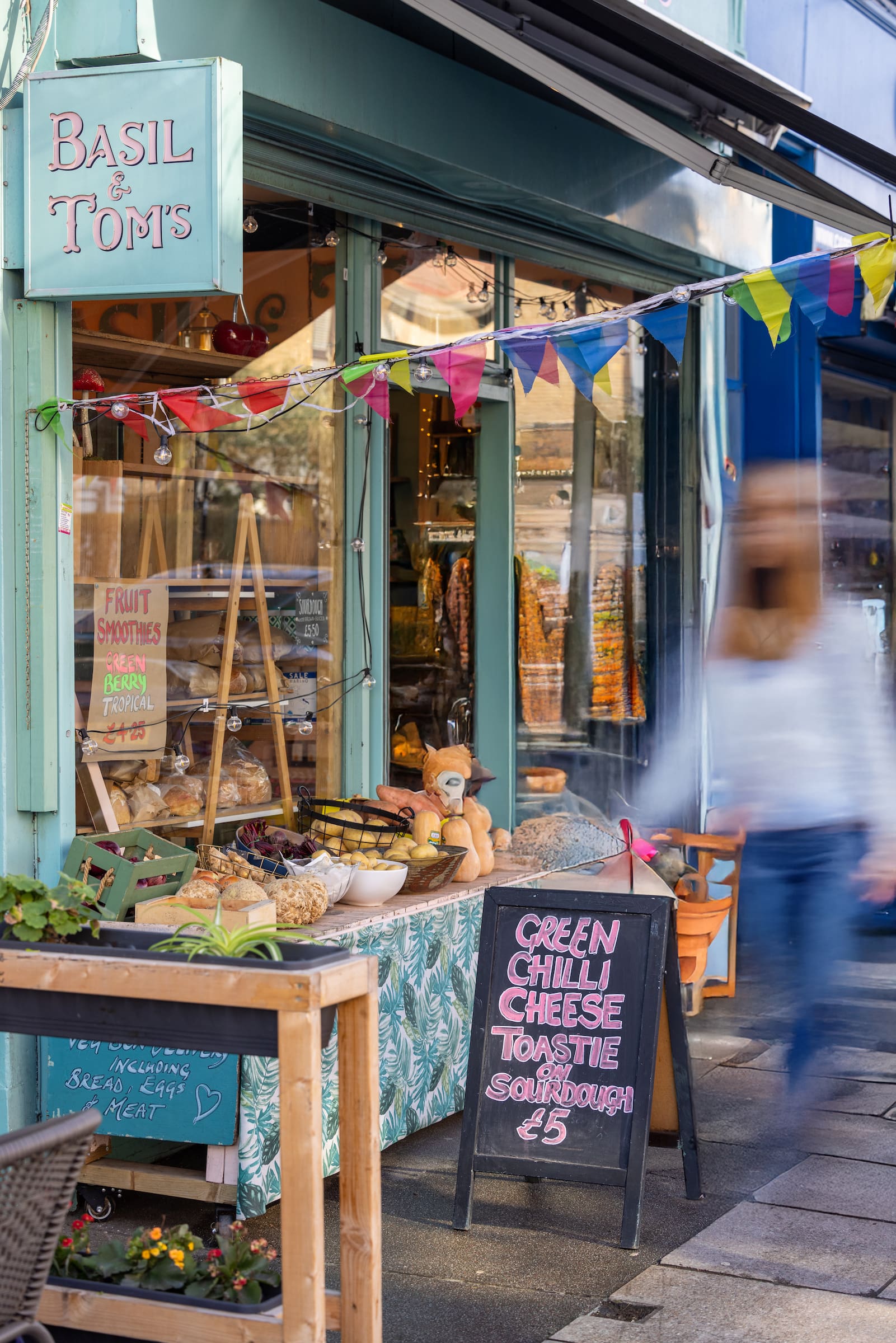 Basil and Tom's storefront in Acton with bunting, fresh bread display, fruit smoothie signs and a chalkboard advertising green chilli cheese toastie on sourdough