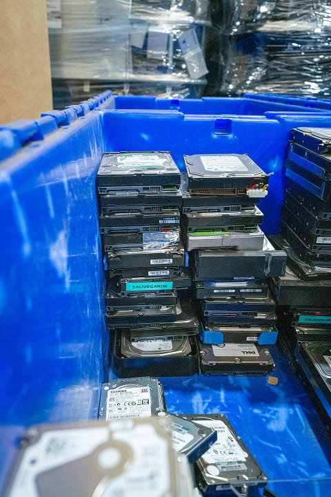Pile de disques durs usagés dans un grand bac en plastique bleu pour recyclage électronique.