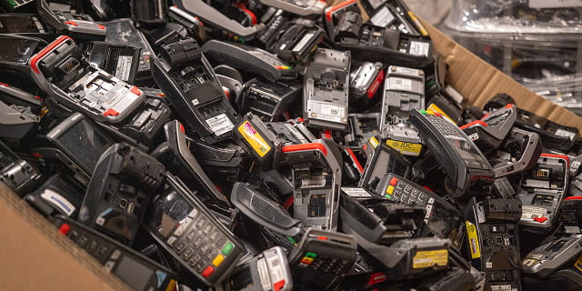 Pile de terminaux de paiement électroniques usagés dans une caisse en carton.