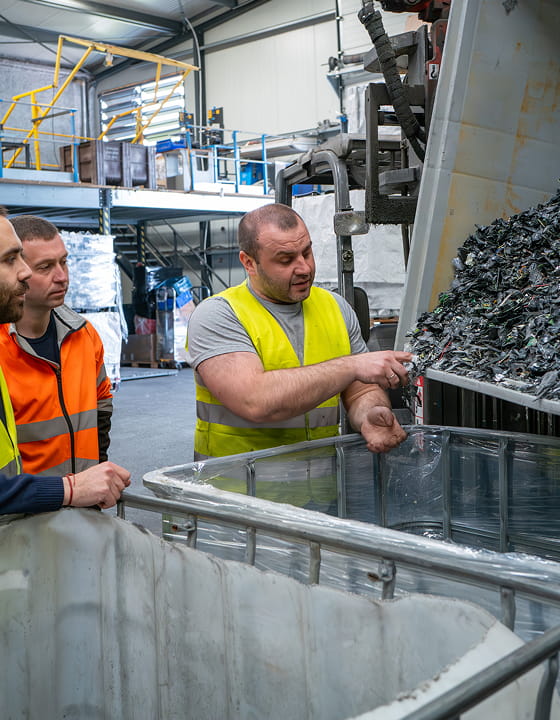 Trois ouvriers en gilets réfléchissants inspectent des matières plastiques dans une usine de recyclage.