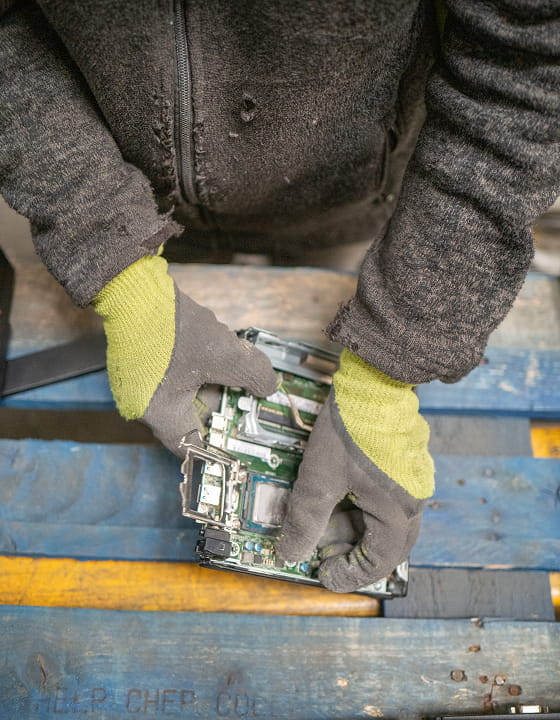 Une personne avec des gants démontant un circuit imprimé sur une palette en bois bleue.