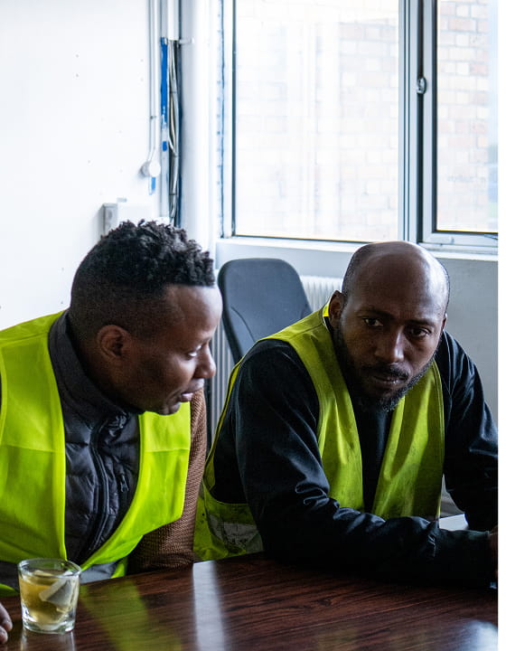 Deux hommes portant des gilets jaunes parlant à une table près d'une fenêtre.
