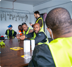Workers in safety vests seated and talking around a table in a meeting room.