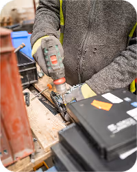 Person using a power drill to work on a mechanical component on a woodworking bench.