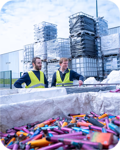 Two men in yellow safety vests standing by a large container full of colorful lighters outdoors.