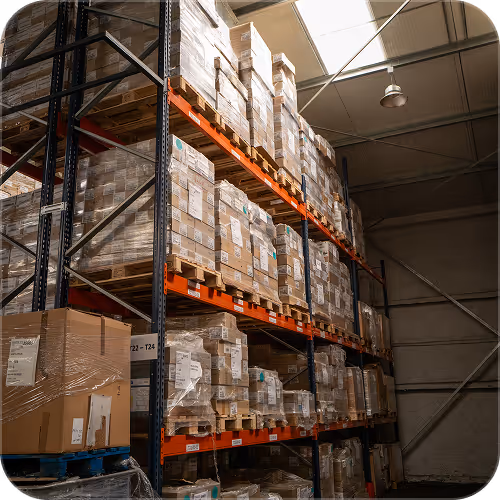 Warehouse shelves stacked with wrapped pallets of boxes under industrial ceiling lights.