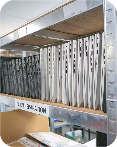 Shelf holding multiple black and white laptops labeled for PC repair in a storage room.