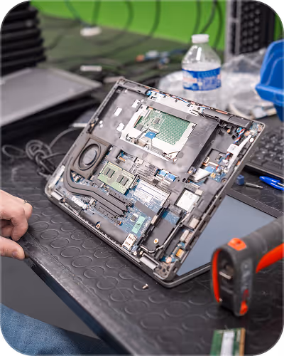 Person repairing a laptop with its back cover removed on a workbench.