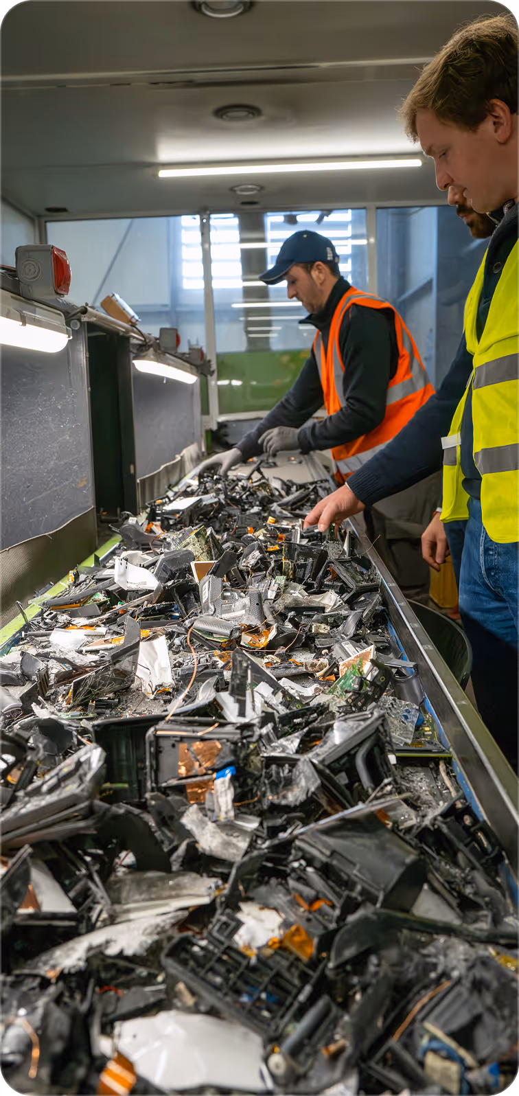 Workers wearing safety vests sorting electronic waste on a conveyor belt in a recycling facility.