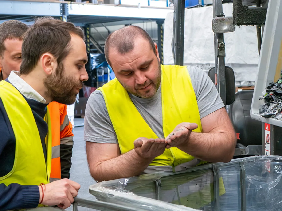 Trois travailleurs portant des gilets de sécurité observent des granulés recyclés dans la main de l'un d'eux.
