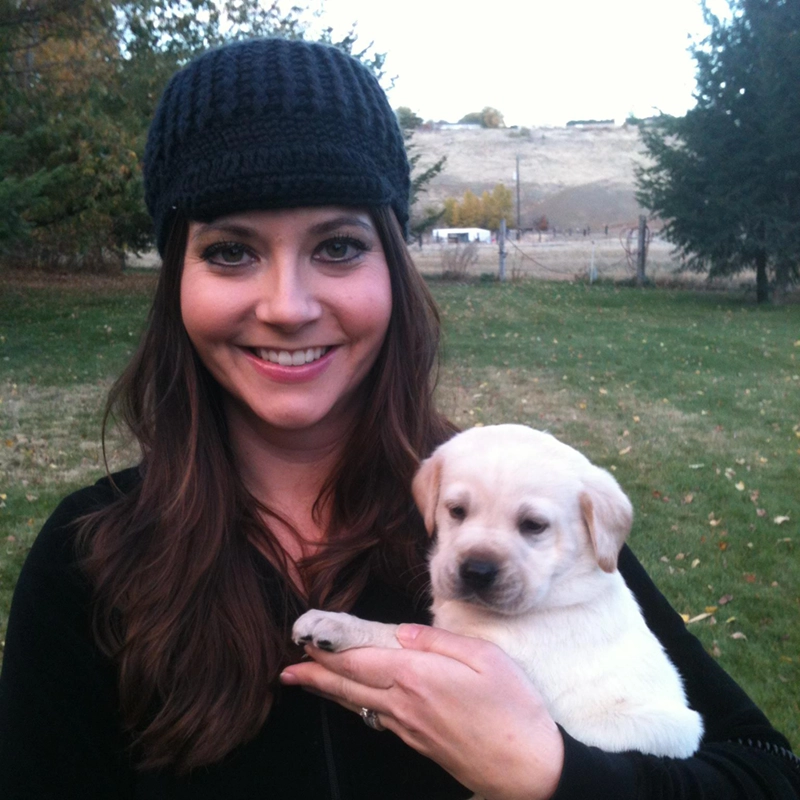 Woman holding a yellow Labrador puppy from Water Walker Labs outdoors with rolling hills in the background.