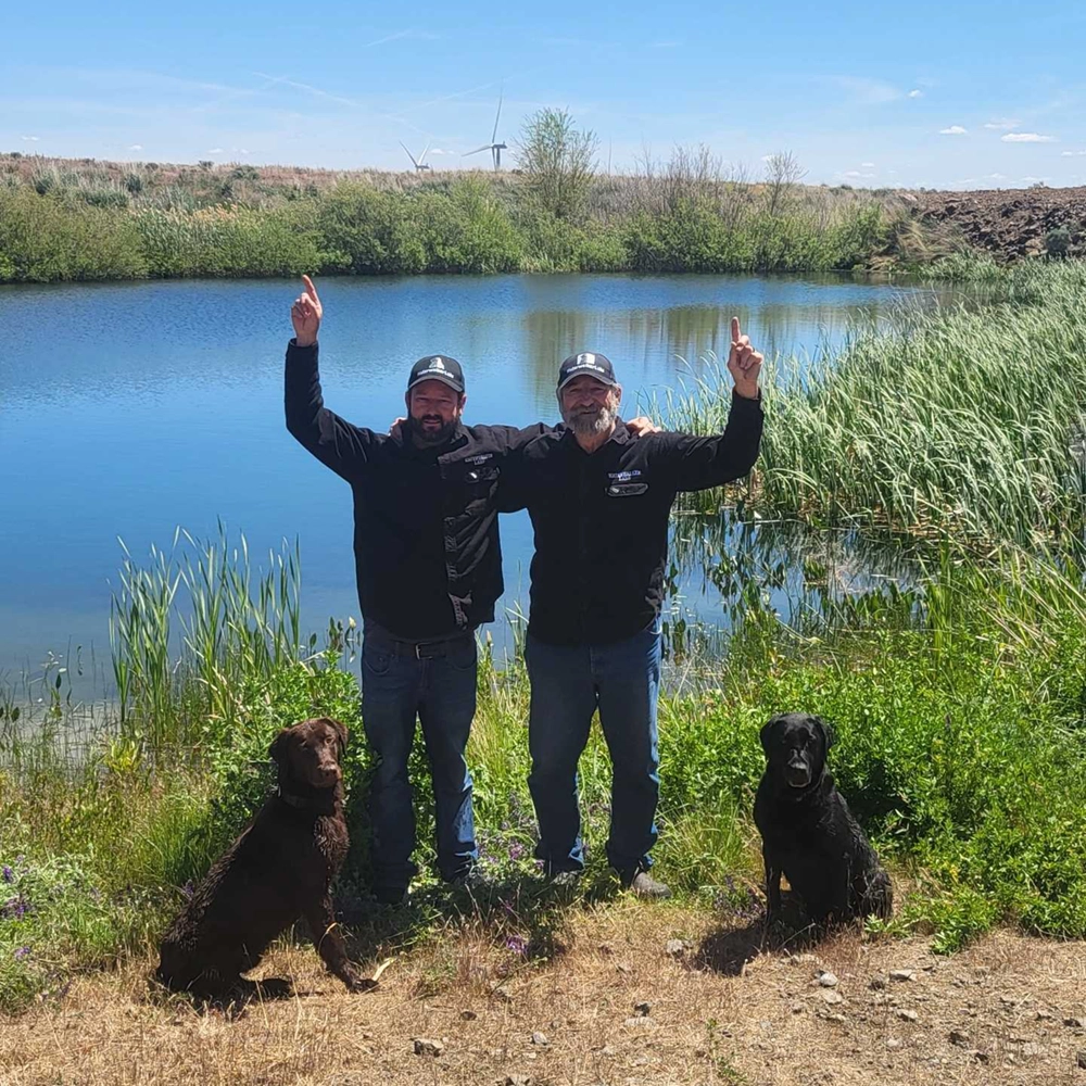 Mark and Jason, father and son with their trusty dogs in front of a pond on their property in Mabon Washington.