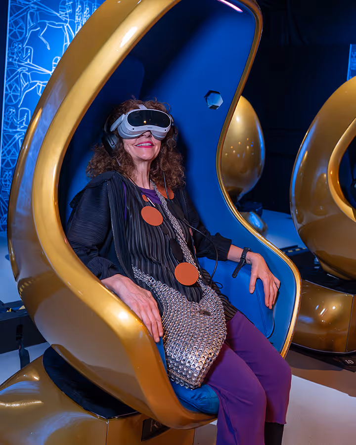 Woman wearing VR headset and headphones sitting in a gold and blue futuristic chair.